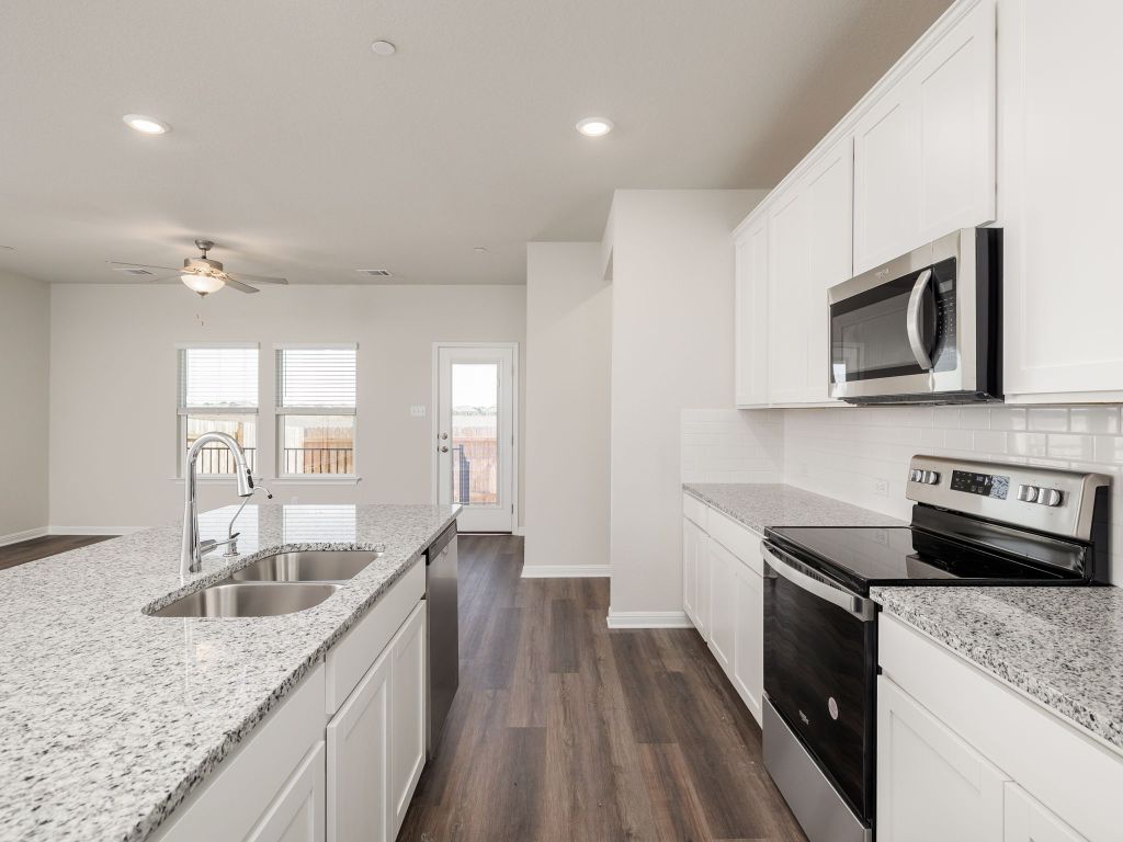 105 Texas Agate Drive, Unit 5 Kyle, TX 78640 - Photo 7 of 19 a kitchen with stainless steel appliances granite countertop a sink dishwasher stove and microwave with wooden floor