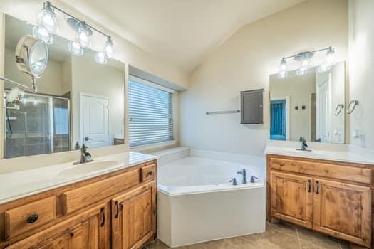 166 Oxford Ranch Road Waxahachie, TX 75167 - Photo 10 of 27 Dual wood-finish vanities with countertop sinks, a built-in corner soaking tub, a separate glass-enclosed shower, and a vaulted ceiling