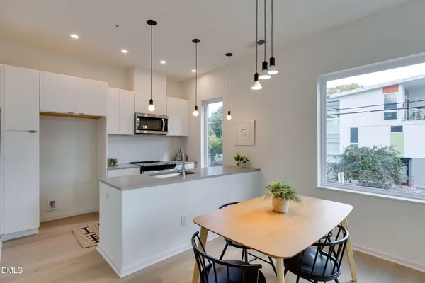 a kitchen with kitchen island a stove a refrigerator a sink a dining table and chairs with wooden floor
