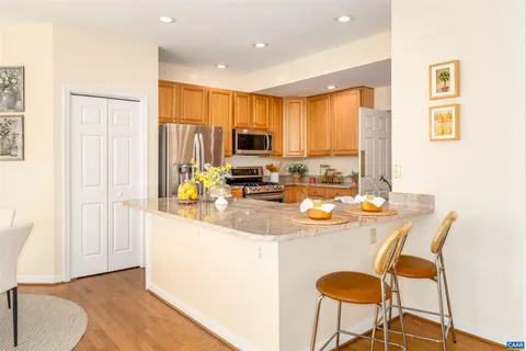 a kitchen with stainless steel appliances granite countertop a stove a refrigerator a sink a dining table and chairs with wooden floor