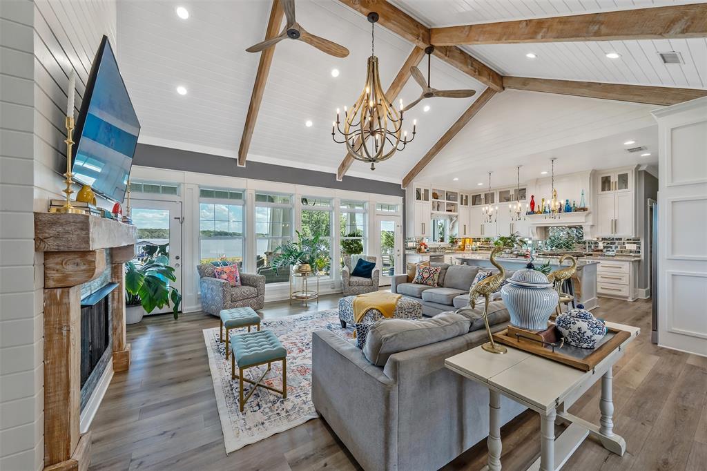 16241 Big Oak Bay Road Tyler, TX 75707 - Photo 6 of 40 Open-concept living space featuring vaulted ceilings with exposed wood beams, a rustic wood mantel fireplace, wood-finish flooring, and a wall of windows