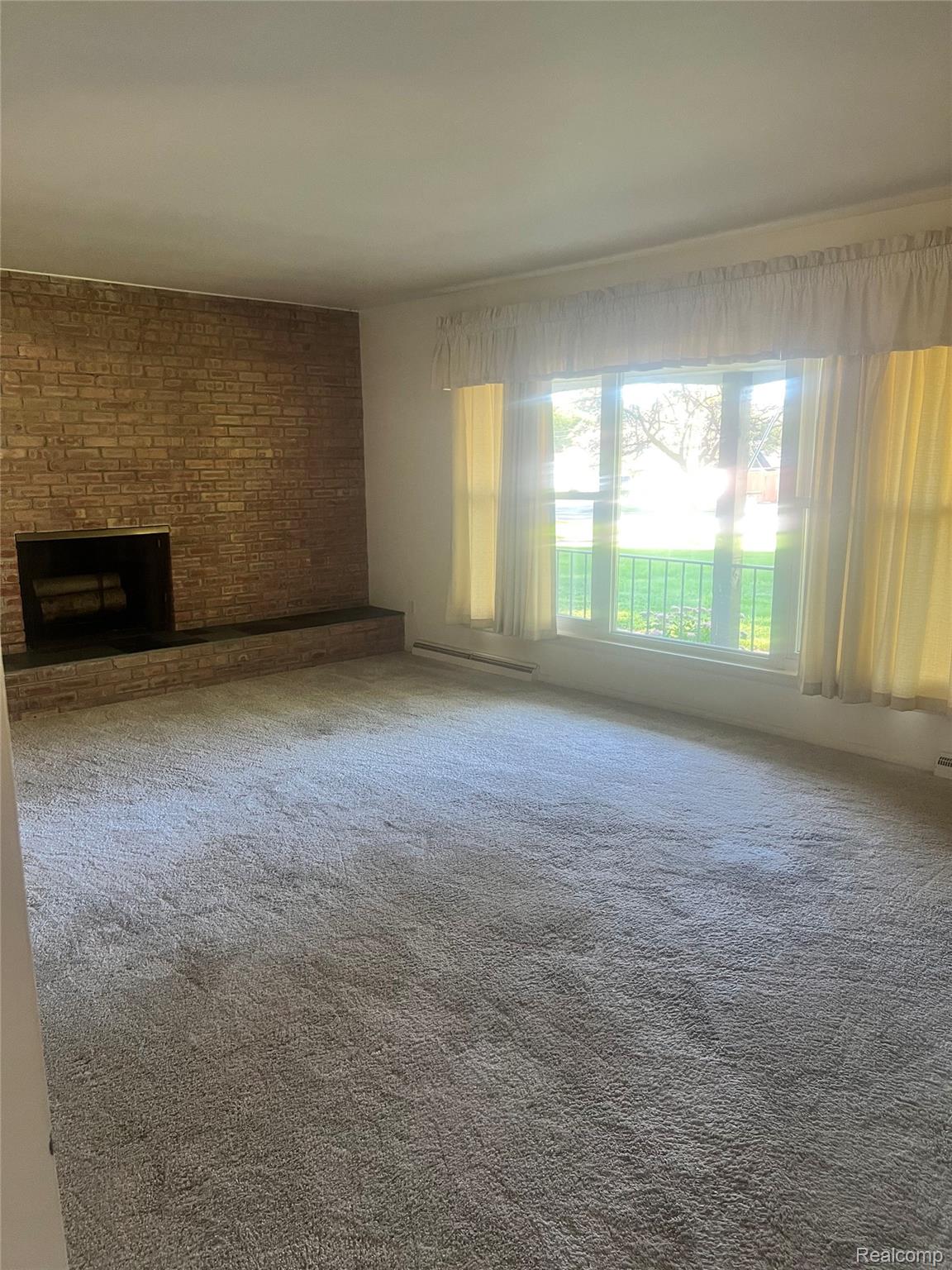 3063 West Britton Road Perry, MI 48872 - Photo 14 of 32 Brick-clad fireplace with hearth, wall-to-wall carpeting, and large windows with horizontal muntins