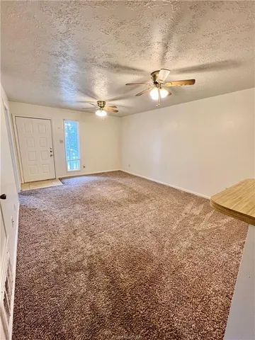 an empty room with a ceiling fan and kitchen view
