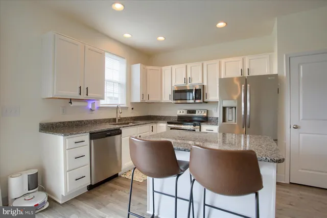 a kitchen with stainless steel appliances granite countertop a stove a sink a refrigerator white cabinets and wooden floor