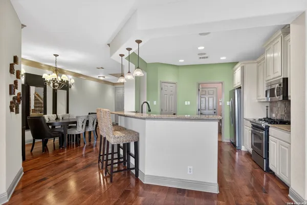 a kitchen with stainless steel appliances kitchen island granite countertop a stove a refrigerator a dining table and chairs with wooden floor