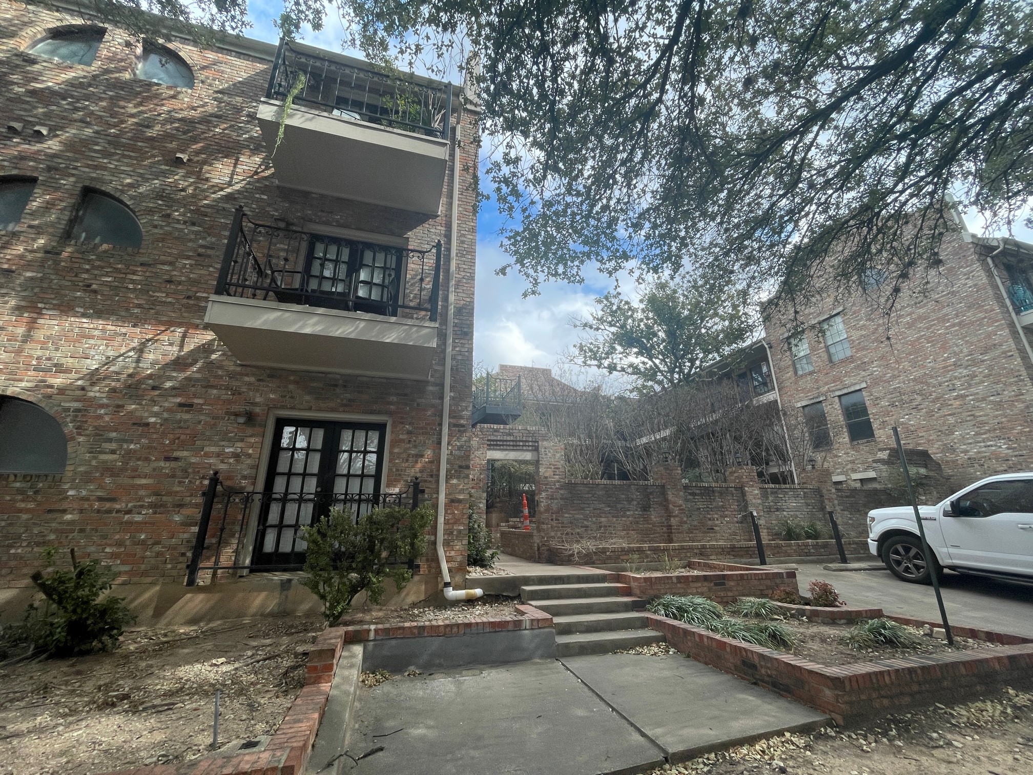 View of side of property featuring a balcony, brick siding, a garden, and french doors