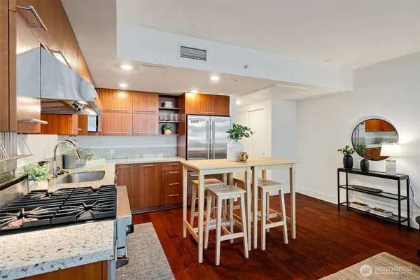 a kitchen with stainless steel appliances granite countertop a stove top oven a sink a dining table and chairs with wooden floor