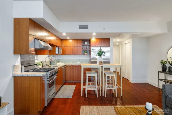 a kitchen with stainless steel appliances granite countertop a stove top oven a sink a dining table and chairs with wooden floor