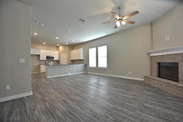 a view of an empty room with wooden floor and a kitchen