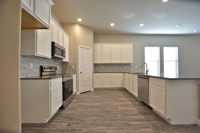 a large kitchen with stainless steel appliances granite countertop a stove a sink and white cabinets