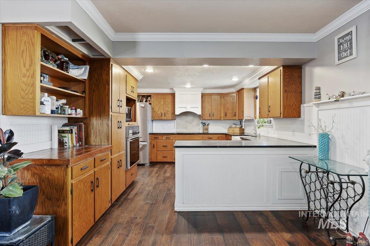 173 Main Line Ranch Road Rupert, ID 83350 - Photo 15 of 47 Kitchen with brown cabinets, dark wood-style floors, crown molding, a peninsula, and open shelves