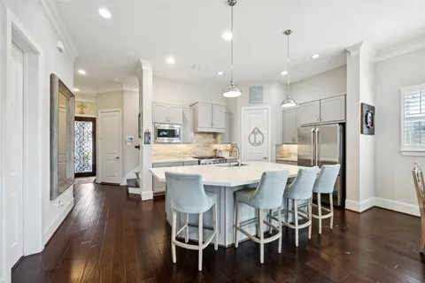 a kitchen with stainless steel appliances kitchen island granite countertop a dining table chairs refrigerator and microwave