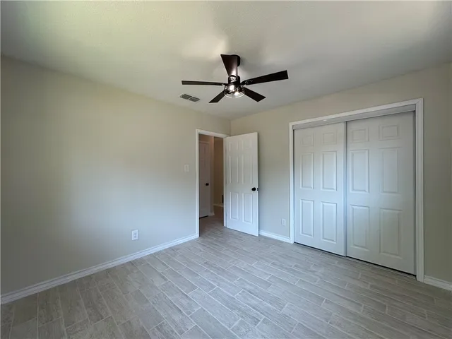 an empty room with wooden floor fan and windows