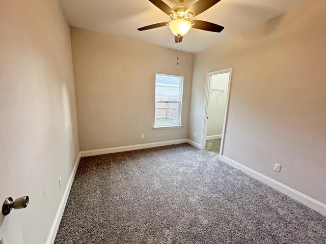 an empty room with a chandelier fan and windows