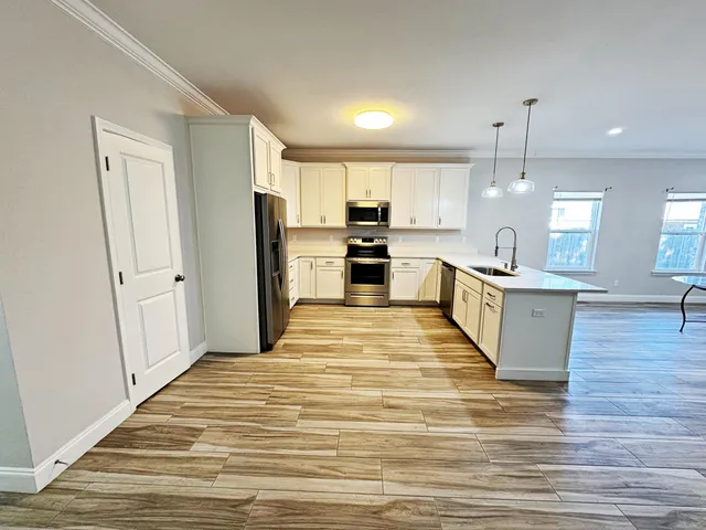 a large kitchen with kitchen island a stove a sink dishwasher a refrigerator and white cabinets with wooden floor