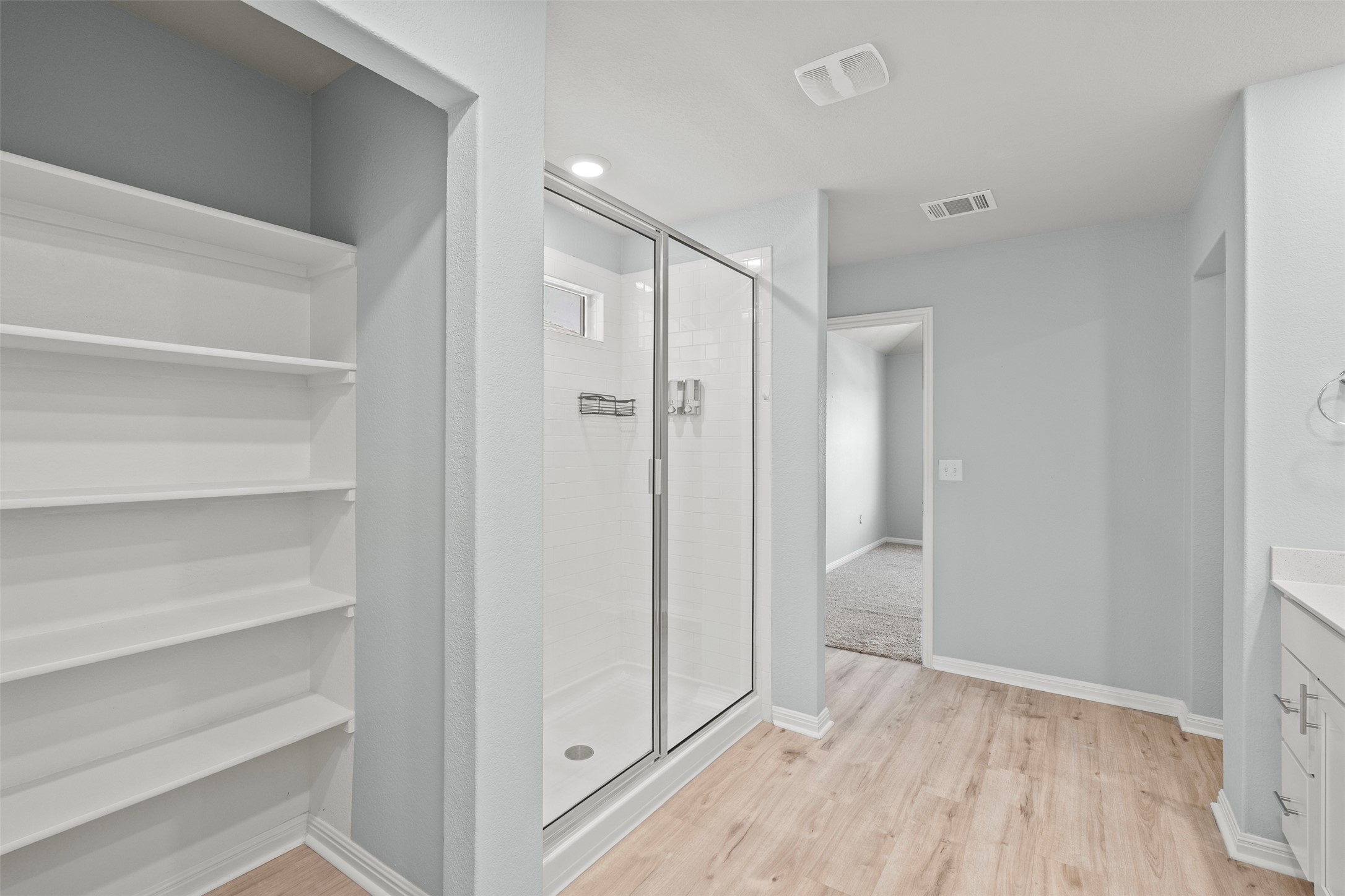 120 Ellinger Road Georgetown, TX 78626 - Photo 24 of 28 Spacious bathroom featuring a glass-enclosed shower, light wood-finish flooring, built-in shelving, white vanity with stone countertop, and light blue wall color