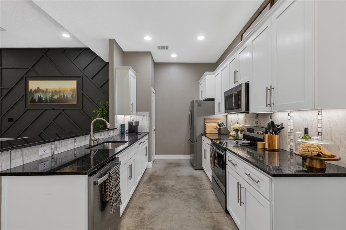 145 Cardinal Loop Paige, TX 78659 - Photo 14 of 40 A well-appointed kitchen features dark granite countertops, crisp white cabinetry, and modern stainless steel appliances.