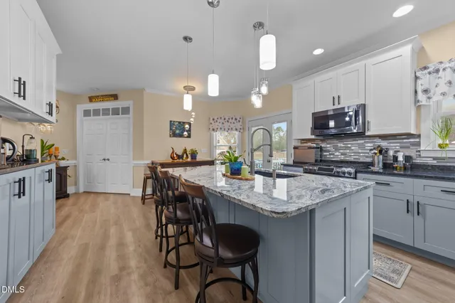 a kitchen with stainless steel appliances kitchen island granite countertop a refrigerator a stove a sink a dining table and chairs with wooden floor