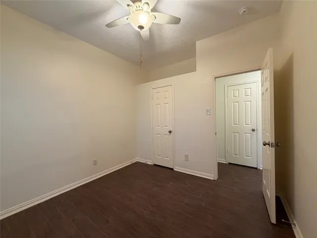 a view of an empty room with wooden floor and a ceiling fan