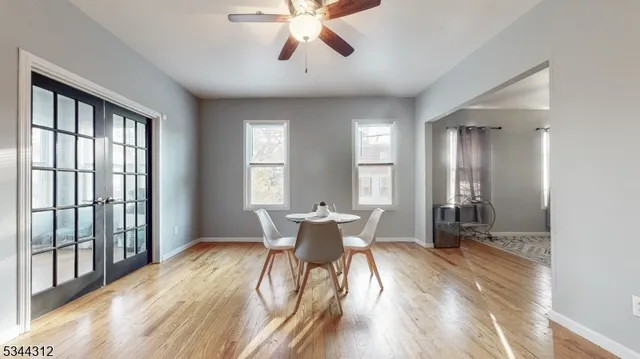 a dining room with wooden floor a chandelier fan a glass table and windows