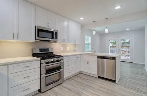 a kitchen with stainless steel appliances granite countertop a stove top oven a sink and white cabinets