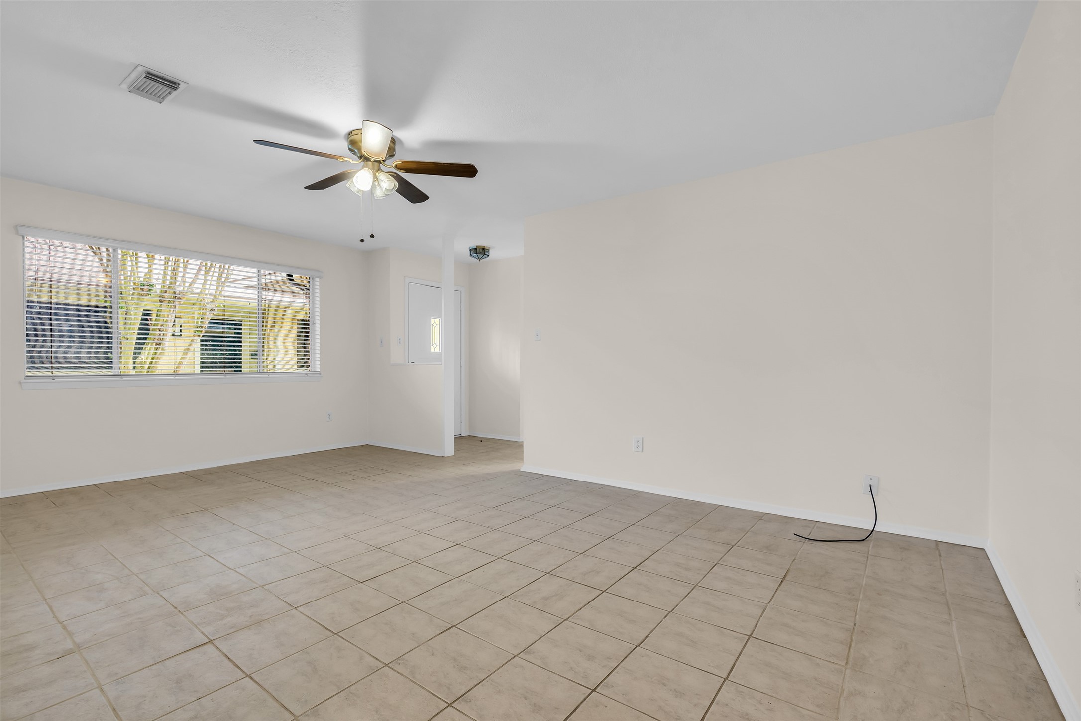 1447 Silverpines Road Houston, TX 77062 - Photo 9 of 17 The living room offers a comfortable, open-concept layout with neutral tile flooring that complements a variety of decorating styles. A ceiling fan provides year-round comfort, while the large window with blinds fills the space with natural light, creating a bright and inviting atmosphere. The functional design allows for easy furniture placement and seamless flow to the adjacent rooms, making it ideal for both everyday living and entertaining.