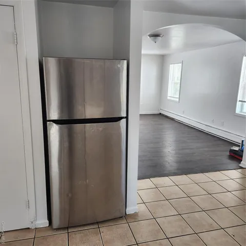 a view of a refrigerator in kitchen and an empty room with wooden floor