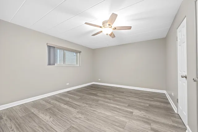 a view of an empty room with wooden floor and a ceiling fan