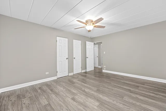 a view of an empty room with chandelier fan and wooden floor