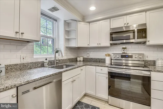 a kitchen with granite countertop a sink stainless steel appliances and white cabinets