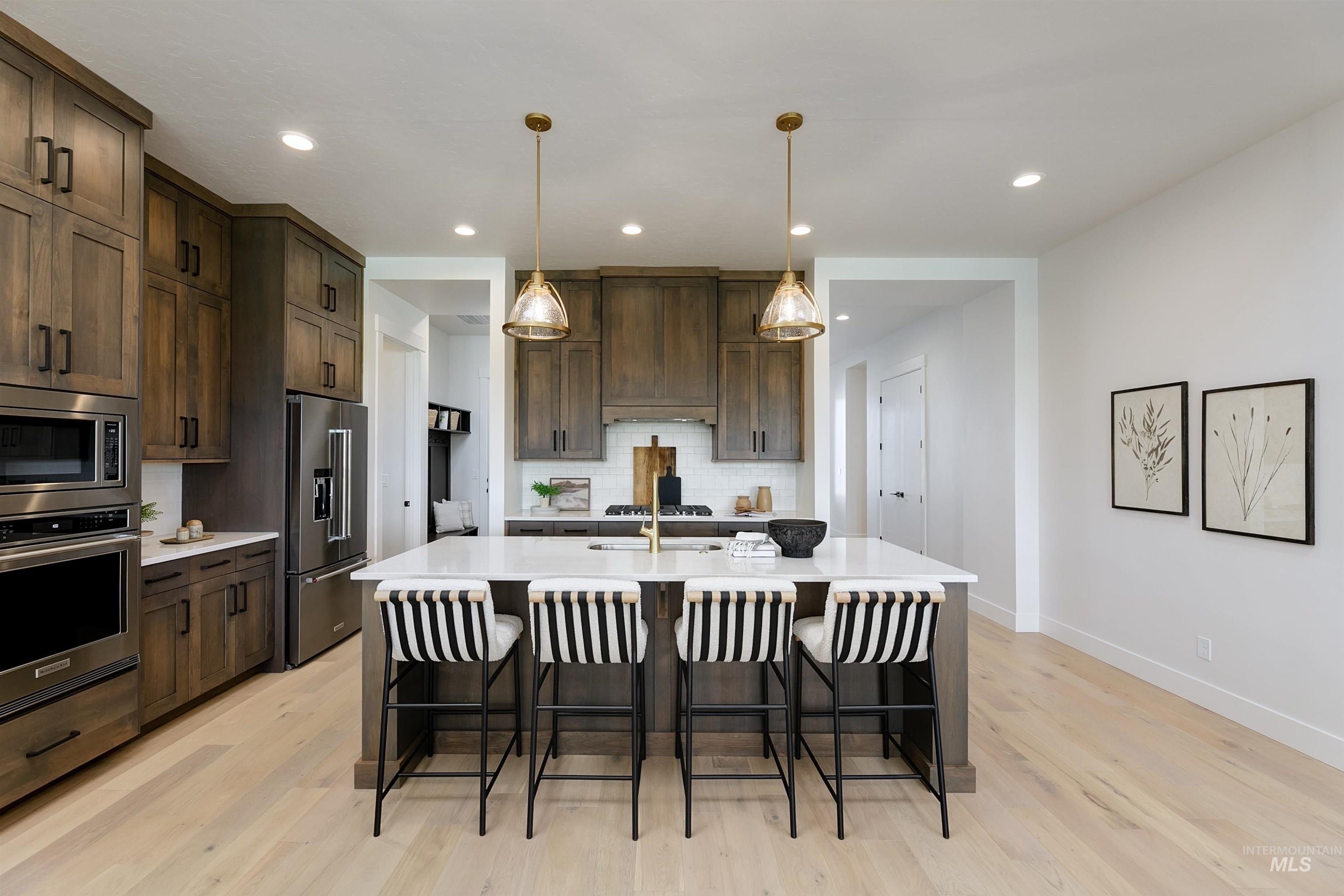 11468 South Saylis Place Kuna, ID 83634 - Photo 6 of 38 Kitchen featuring dark wood finish cabinetry, a breakfast bar area, stainless steel appliances, a kitchen island with sink, and hanging light fixtures