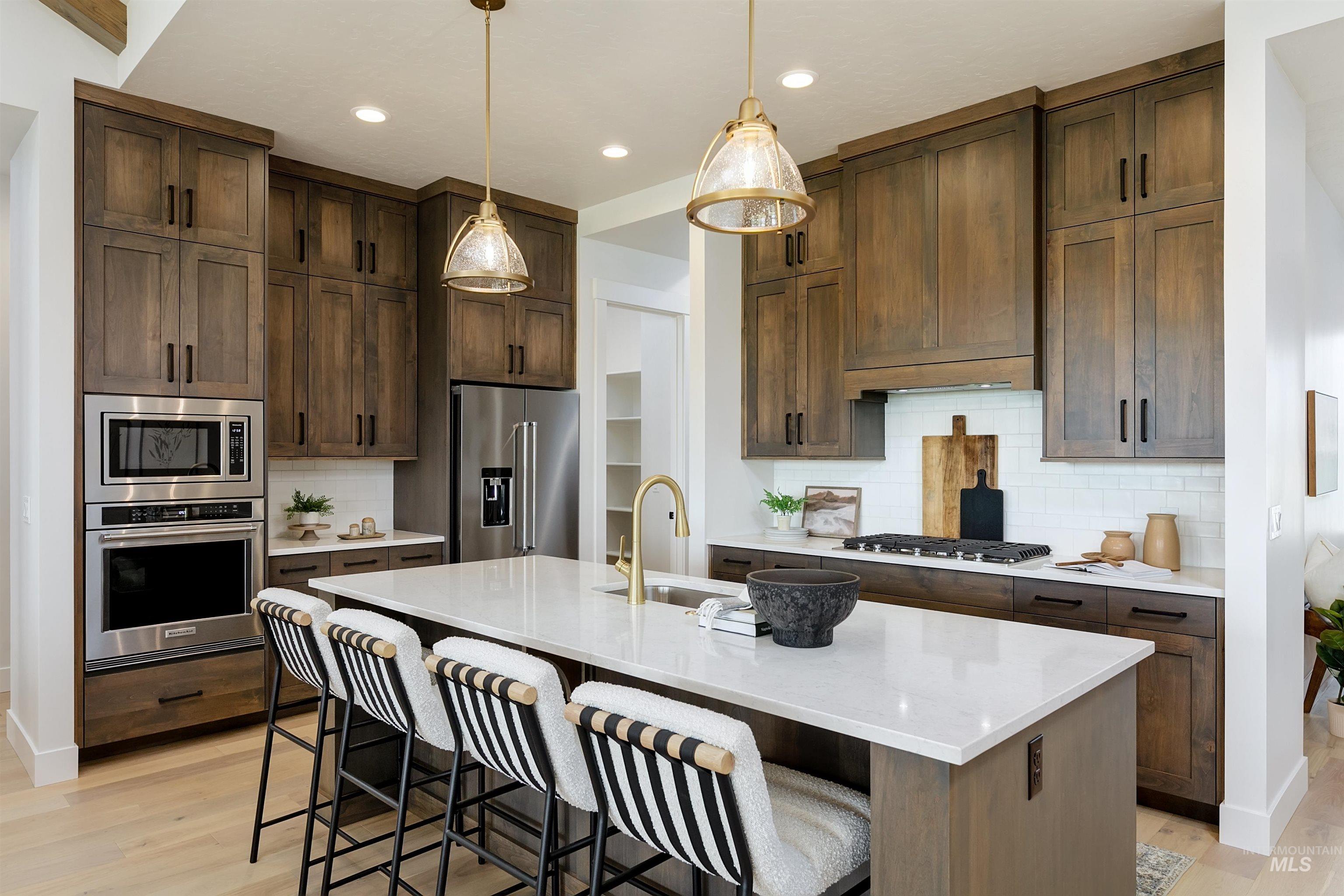 11468 South Saylis Place Kuna, ID 83634 - Photo 7 of 38 Kitchen featuring tasteful backsplash, a kitchen island with sink, stainless steel appliances, light wood-style floors, and dark wood finish cabinets