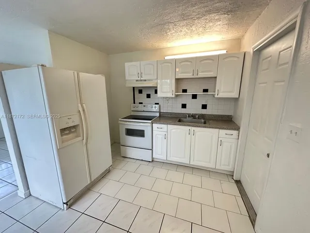 a kitchen with white cabinets a sink a stove a refrigerator and a window