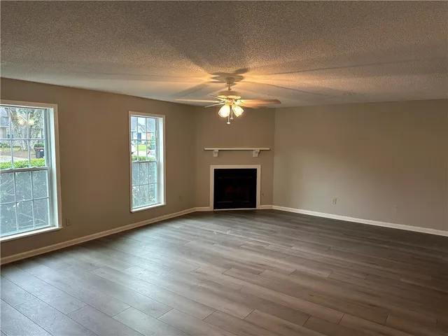 an empty room with wooden floor fireplace and windows