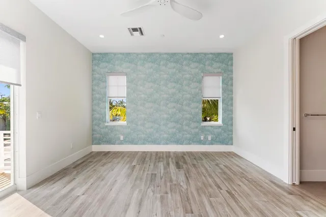 an empty room with wooden floor chandelier fan and windows