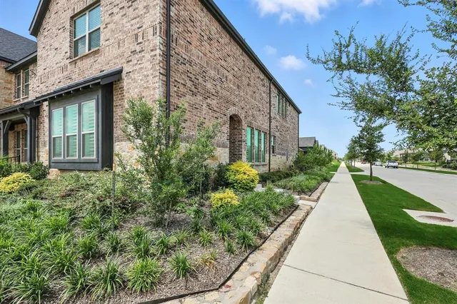 a view of a brick house with a small yard plants and a large tree