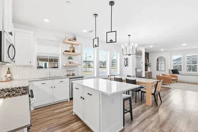 a large white kitchen with granite countertop a stove a sink dishwasher and a dining table with wooden floor
