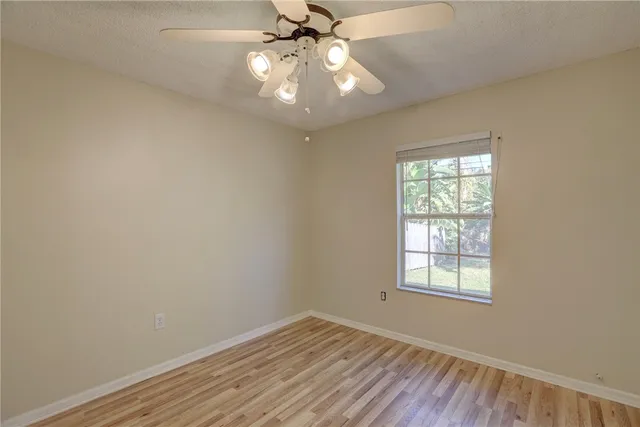 an empty room with wooden floor chandelier fan and windows