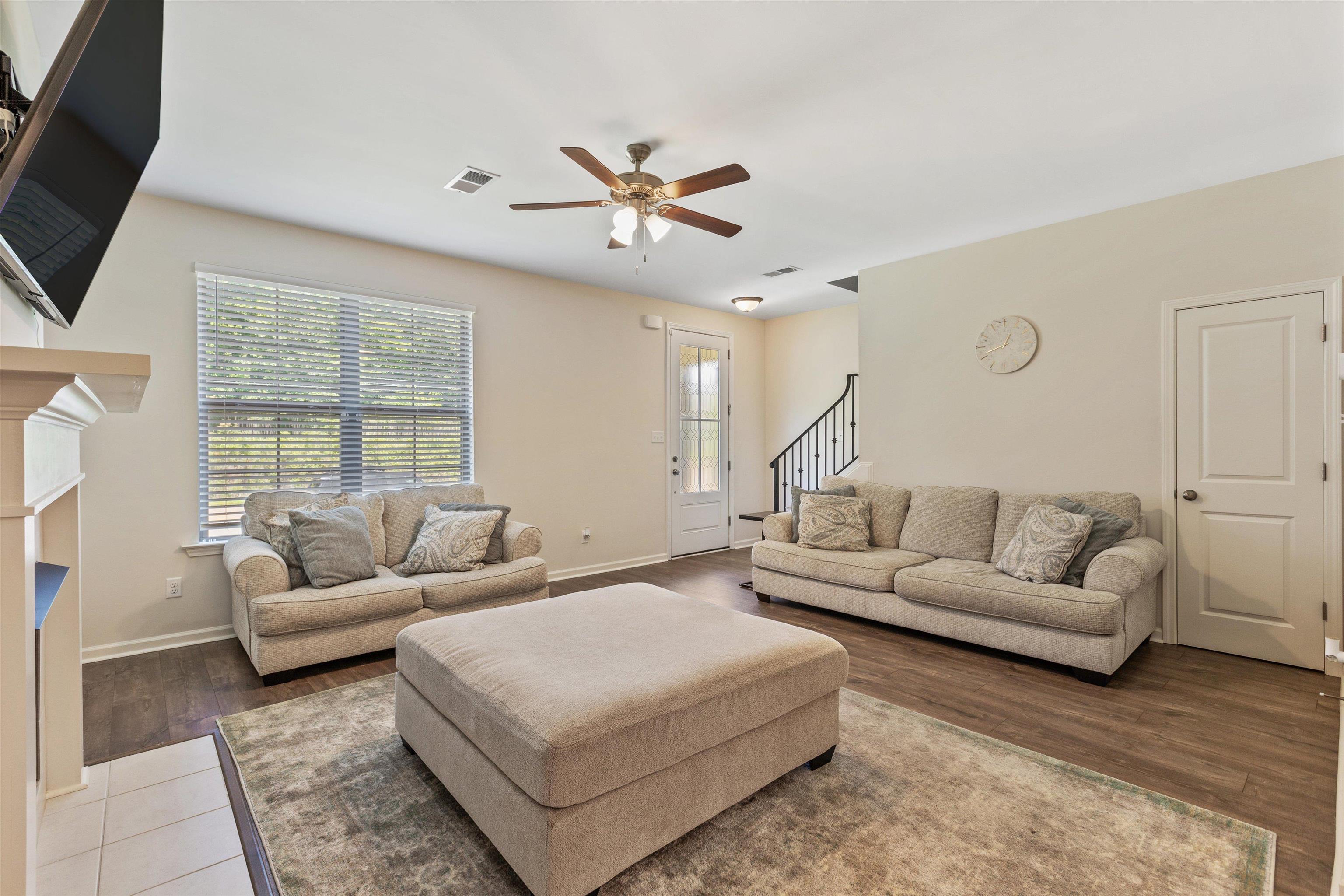 10139 Macon Road Cordova, TN 38018 - Photo 7 of 31 Spacious living area featuring wood-finish flooring, a ceiling fan with integrated lighting, a substantial window with blinds, a white paneled interior door, and a staircase with dark wrought iron spindles