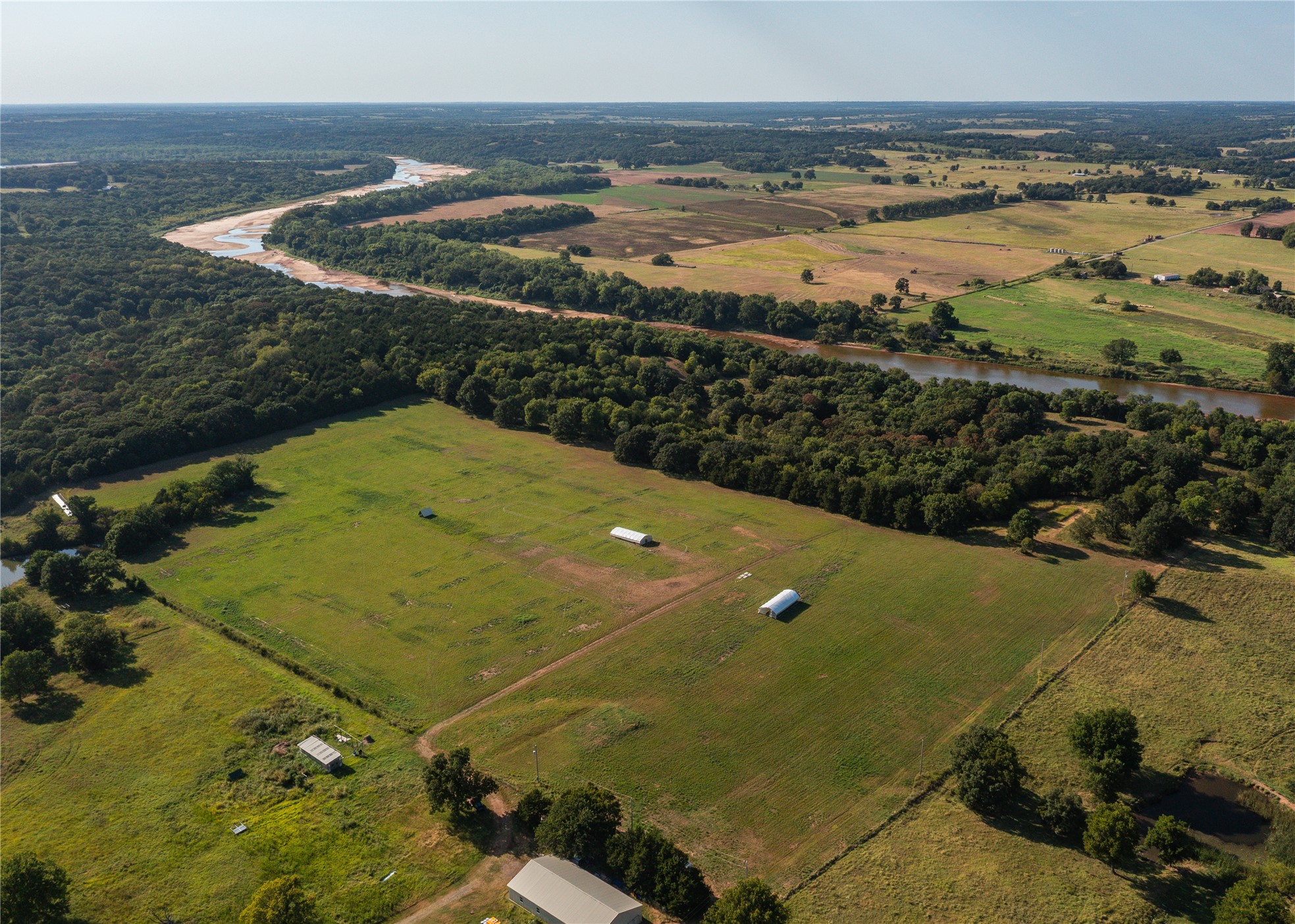 0 West Dunkin Road Cushing, OK 74023 - Photo 4 of 62 Expansive rural landscape featuring a winding river, verdant fields, wooded areas, and multiple agricultural structures