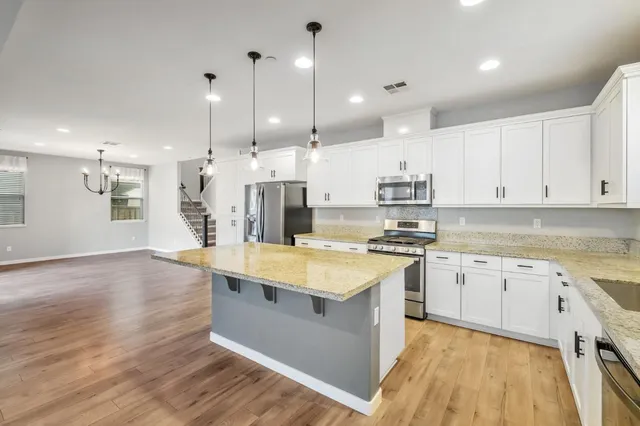 a large kitchen with stainless steel appliances granite countertop a stove top oven a sink dishwasher and a refrigerator with wooden floor