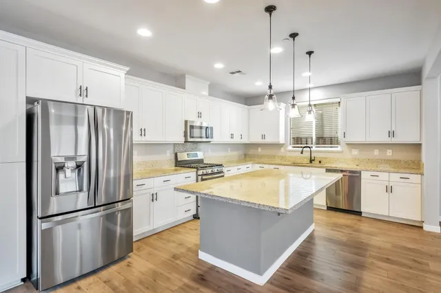 a large kitchen with stainless steel appliances granite countertop a refrigerator a sink dishwasher a stove and white cabinets with wooden floor