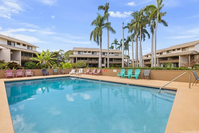 a view of a swimming pool with a lawn chairs under palm trees
