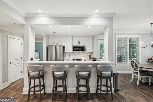 a kitchen with stainless steel appliances kitchen island granite countertop a dining table chairs and white cabinets