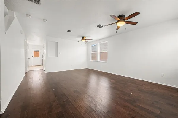 an empty room with wooden floor fan and windows
