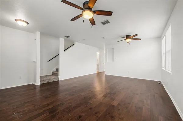 an empty room with wooden floor ceiling fan and window