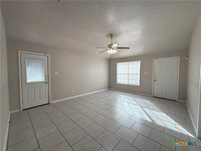 a view of an empty room with window and chandelier fan