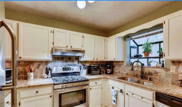 a kitchen with stainless steel appliances granite countertop a stove a sink and white cabinets