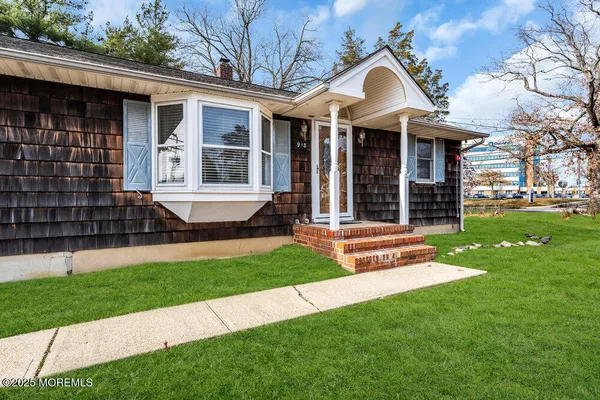 a view of a brick house with a large window and a yard with plants and large tree