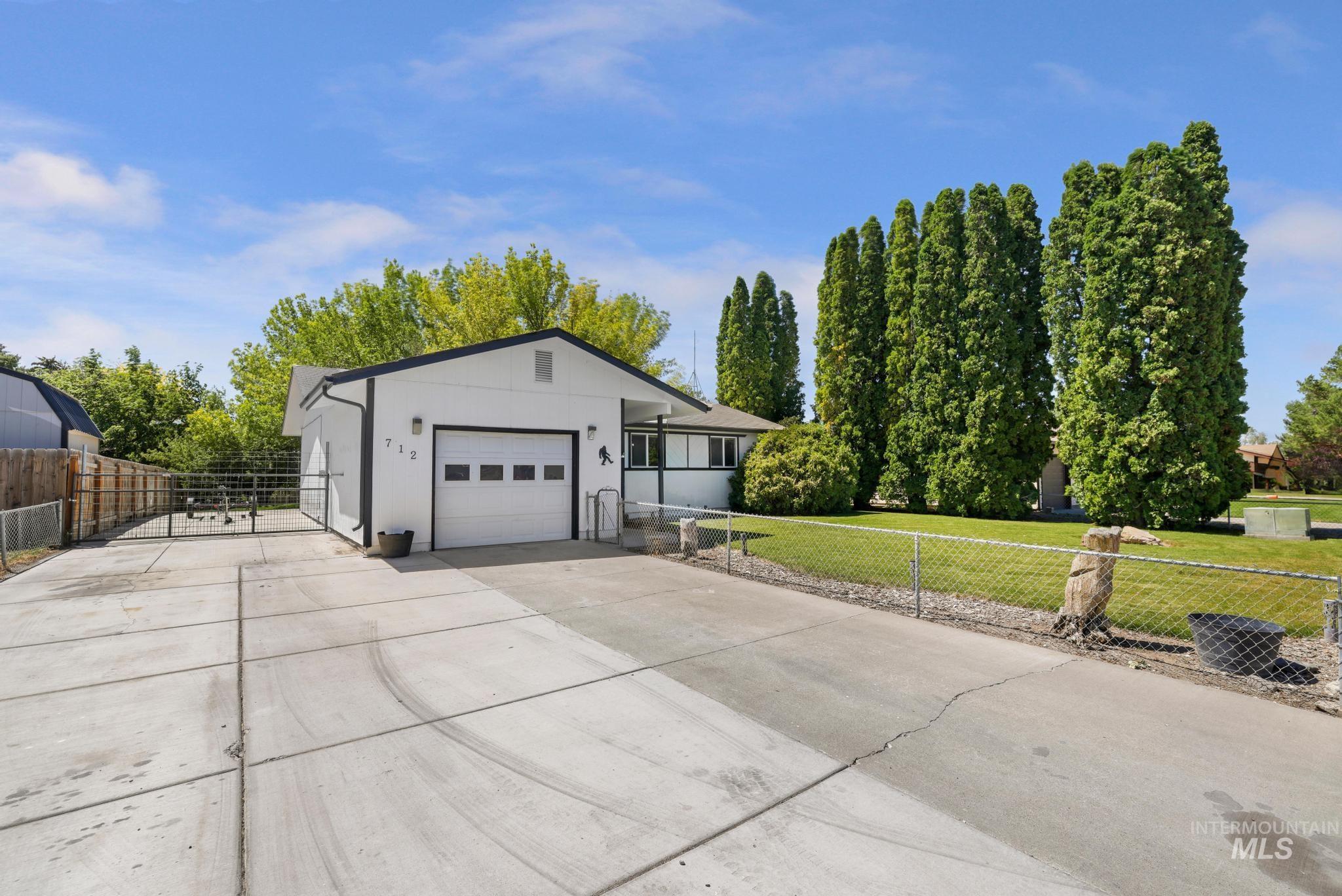 712 Locust Street Kimberly, ID 83341 - Photo 2 of 26 Single-story residence featuring a two-tone exterior with dark trim and a white facade, an attached garage with a panel door, a concrete driveway, a front lawn with mature landscaping, and a fenced side yard